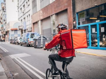 A food delivery worker on a bike with a large backpack on.