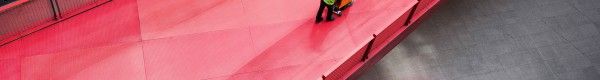 Overhead view of male cleaner pushing industrial floor polisher along long red walkway