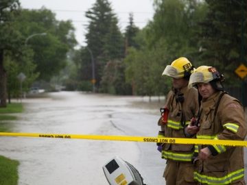 Two Calgary firefighters stand at the scene of a flood.