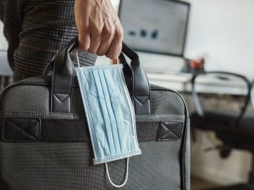 Close-up of a hand holding a surgical mask and a laptop case