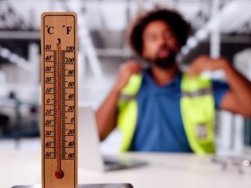 A warehouse worker tries to cool himself. A thermometer is in the foreground.
