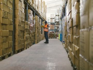 A warehouse worker looks at a tablet among stacks of boxes