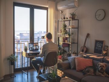A man sits at a desk on a video call in his apartment's living room.