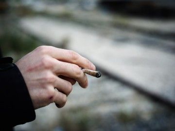 A close-up of a man's hand, holding a joint
