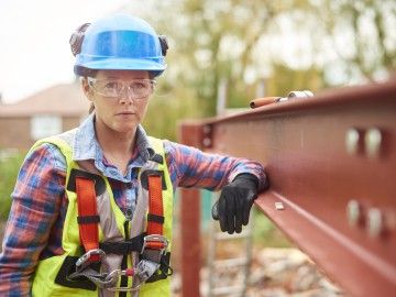 A female construction worker stands next to a steel girder