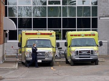 A paramedic wearing a face mask stands next to two ambulances 