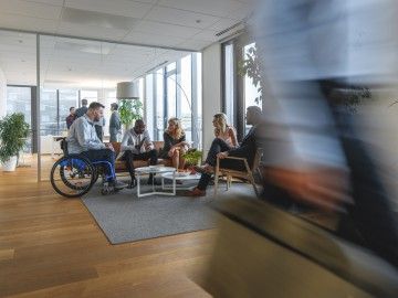 A worker in a wheelchair sits with colleagues in a busy office 