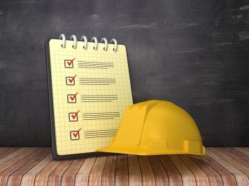 A hard hat, placed next to a check list, against a black background
