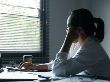 A woman working at a laptop looks out the window with her head resting on her hand