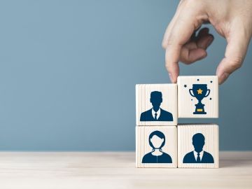 Blocks with workers' silhouettes, one with a trophy is picked up by a hand.