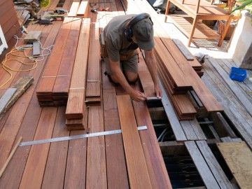 A man kneels as he works with decking boards on a patio