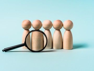 A magnifying glass is positioned in front of a row of five wooden figures