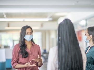 Three women wearing masks talking to each other at work