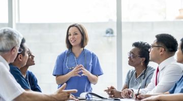 Members of a hospital committee listen to presentation by female health care worker