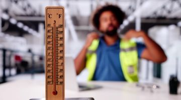 A warehouse worker tries to cool himself. A thermometer is in the foreground.