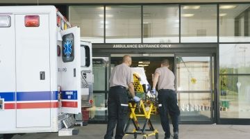 Paramedics wheel a stretcher out of a ambulance in front of a hospital.