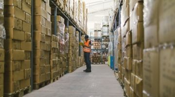 A warehouse worker looks at a tablet among stacks of boxes
