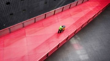 Overhead view of male cleaner pushing industrial floor polisher along long red walkway