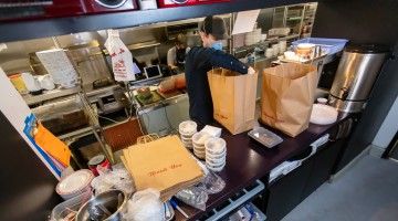 Masked restaurant worker prepares take-out food orders