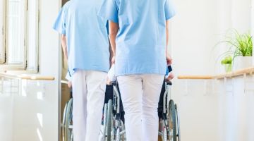 Back of two nursing home employees pushing wheelchair