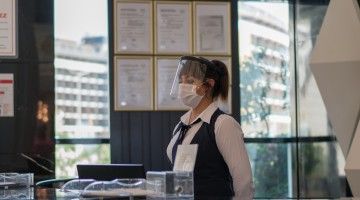 A masked young woman works at a hotel reception desk
