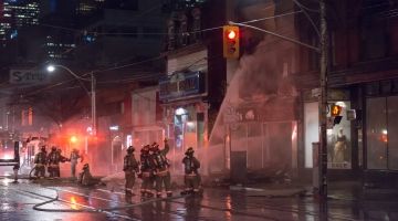 A group of firefighters aim a firehose at a building