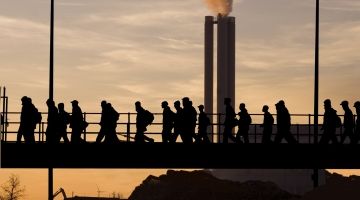 Silhouette of industrial workers crossing a bridge in front of a smoke stack