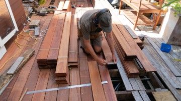 A man kneels as he works with decking boards on a patio