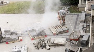 A worker bends over, cutting paving stones in a landscaping job