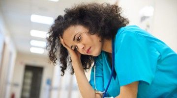 A nurse sits in deserted hospital hallway, looking worried