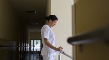 A downcast nurse in a dark hallway looks to an exit