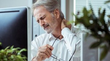 Businessman at computer rubbing neck in pain Thumbnail