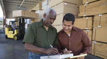 Two workers in a warehouse consult document