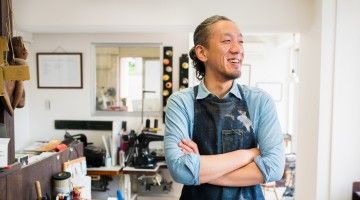 Japanese craftsperson stands in front of his workstation, smiling