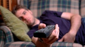 Young adult with remote in his hand, laying on couch watching television