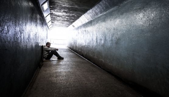 A homeless young man sits on the ground, in a tunnel