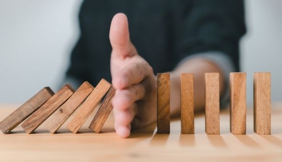 A line of blocks tipping over, a hand stops them from falling.