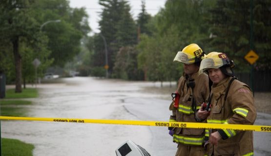Two Calgary firefighters stand at the scene of a flood.