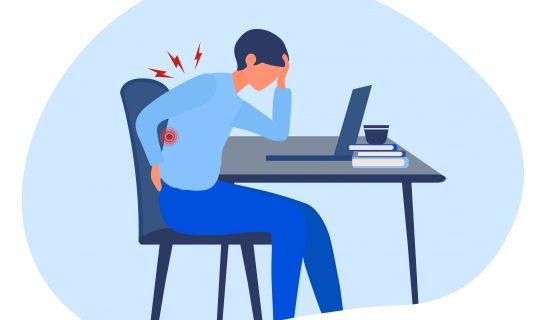 A worker sits hunched over at their desk with pain in their back