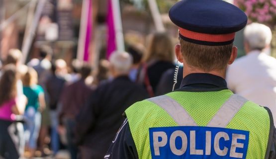 A police officer with their back turned faces a group of people walking around.