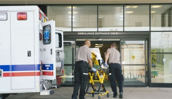 Paramedics wheel a stretcher out of a ambulance in front of a hospital.