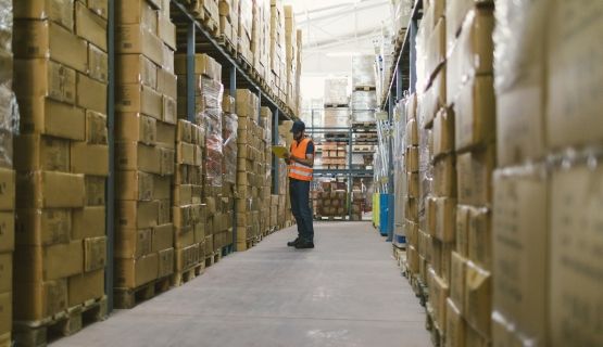 A warehouse worker looks at a tablet among stacks of boxes