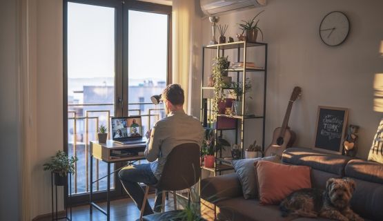 A man sits at a desk on a video call in his apartment's living room.
