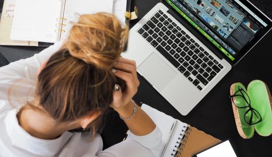 An overhead shot of a woman holding her head in front of a laptop