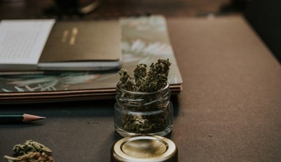 A jar of cannabis buds on a brown desk