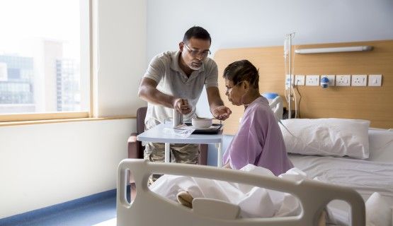 A man feeds his mom at a hospital bedside