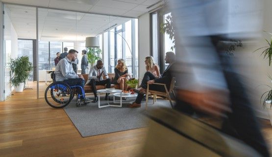 A worker in a wheelchair sits with colleagues in a busy office
