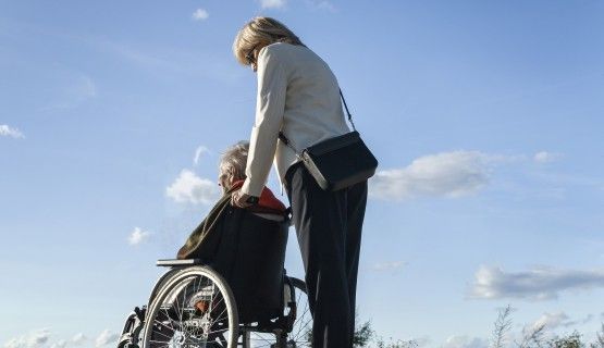 A professional woman pushes an older person in a wheelchair in the outdoors