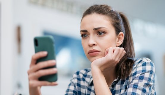 A young woman looks at her phone in frustration and exasperation
