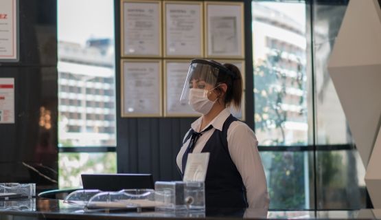 A masked young woman works at a hotel reception desk